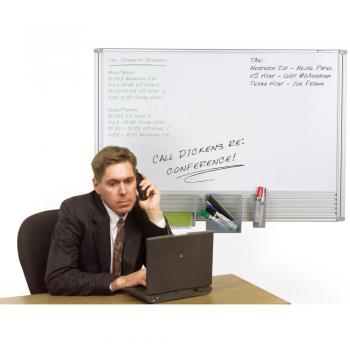 A man sits at an office desk in front of a small white board.