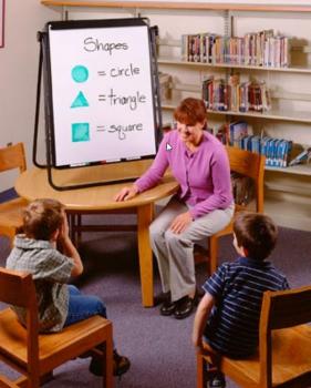 A teacher is in a library with her students, looking at a portable marker board.