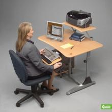 A woman is seated at a sit down or stand up adjustable computer workstation.