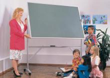 A teacher in s classroom standing in front of a green chalkboard easel.