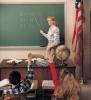 A teacher is shown teaching students in front of a green school blackboard with a full length accessory tray.